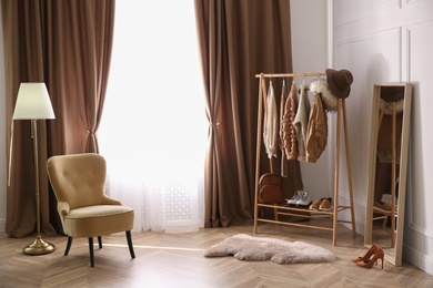 Comfortable armchair and rack near window with stylish curtains in room. Interior design