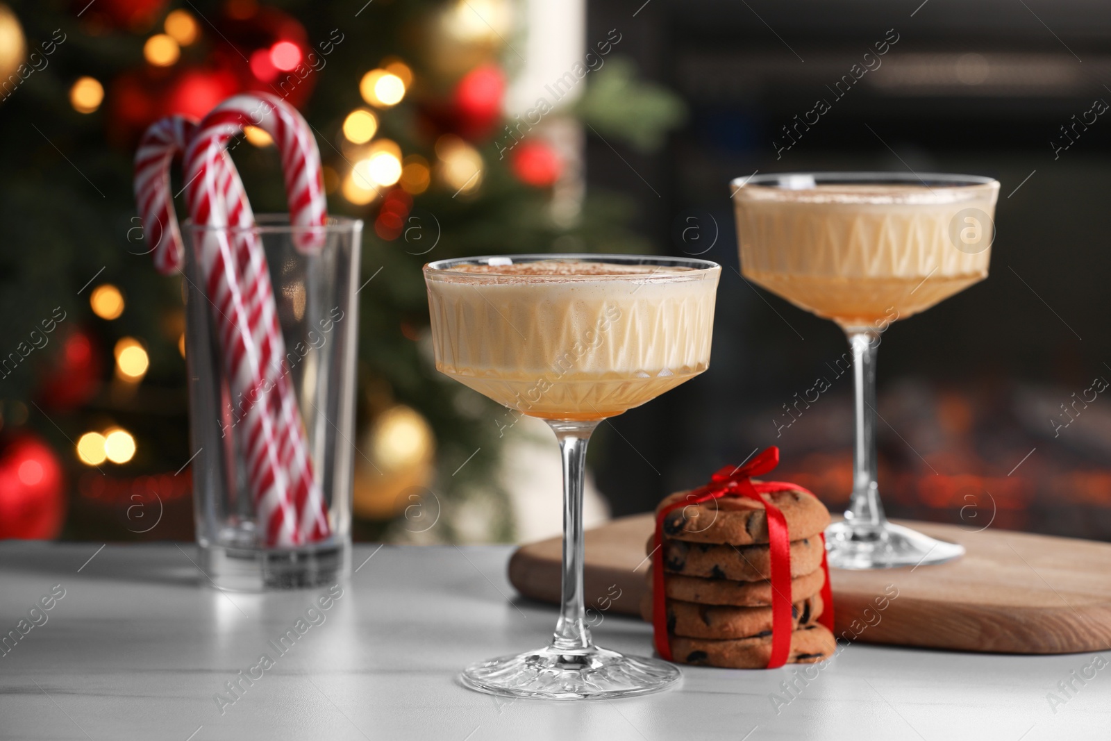 Photo of Tasty eggnog, cookies and candy canes on white marble table against blurred festive lights