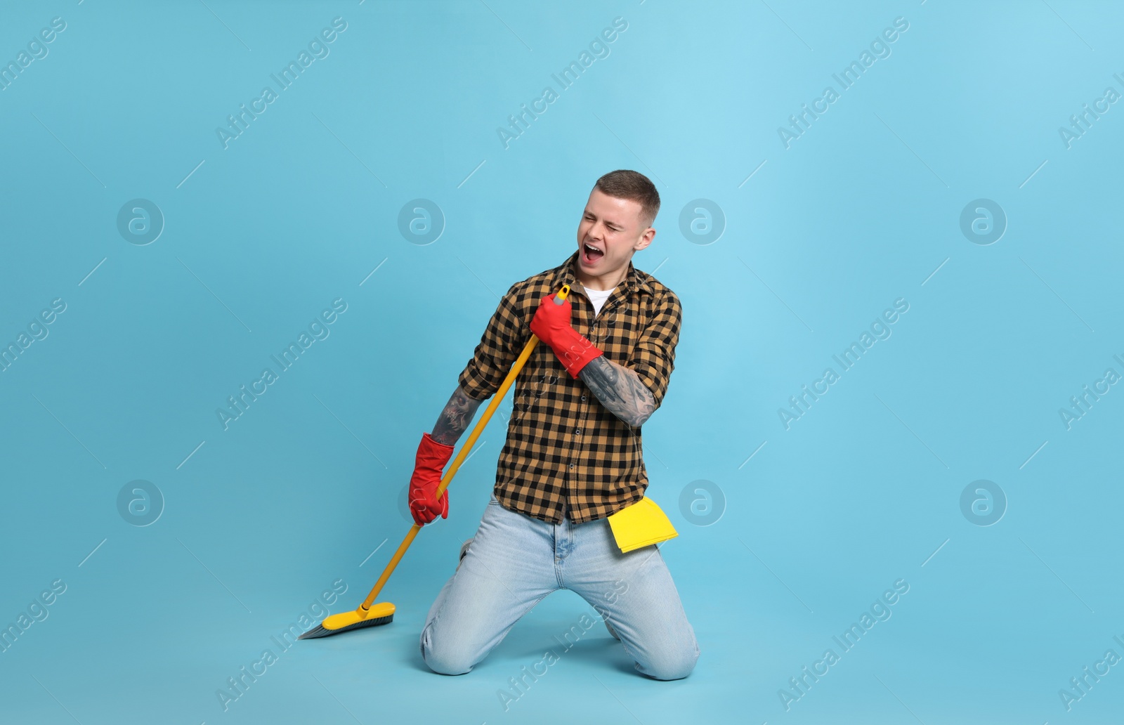 Photo of Handsome young man with floor brush singing on light blue background