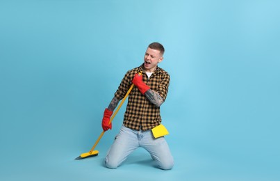 Photo of Handsome young man with floor brush singing on light blue background