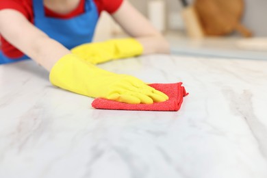Photo of Woman cleaning white marble table with rag in kitchen, closeup