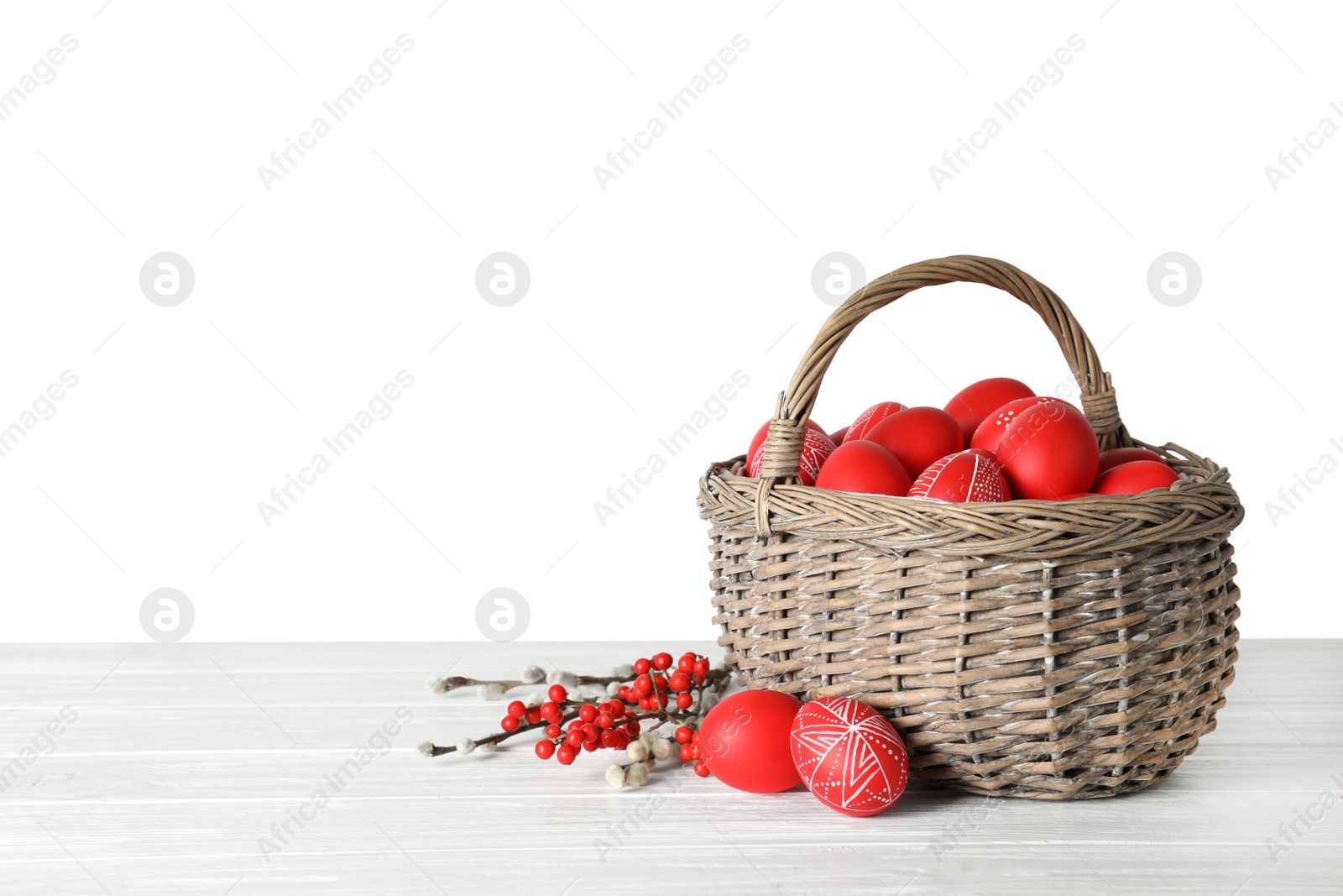 Photo of Wicker basket with painted red Easter eggs on table against white background, space for text