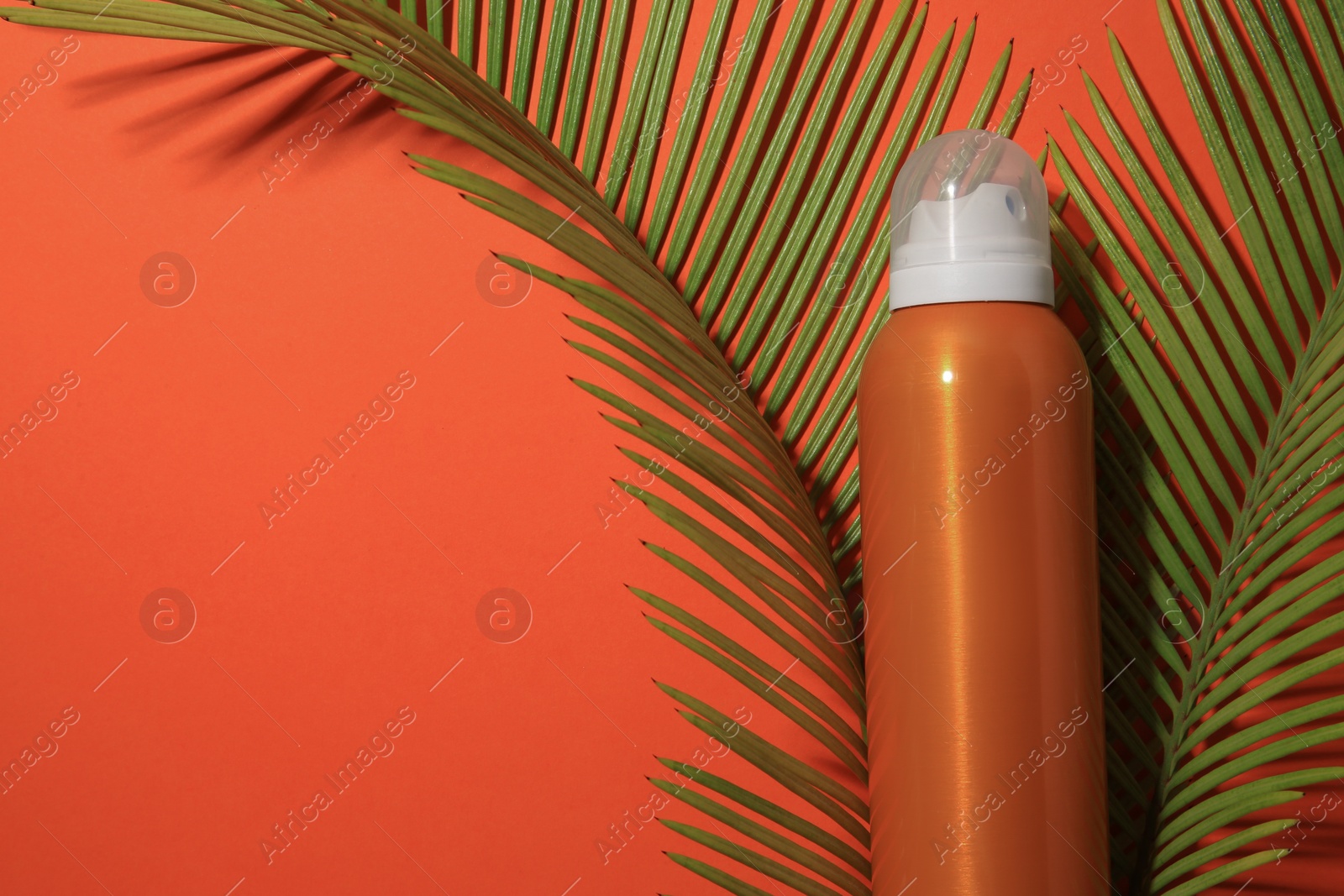 Photo of Sunscreen and tropical leaves on coral background, flat lay and space for text. Sun protection care