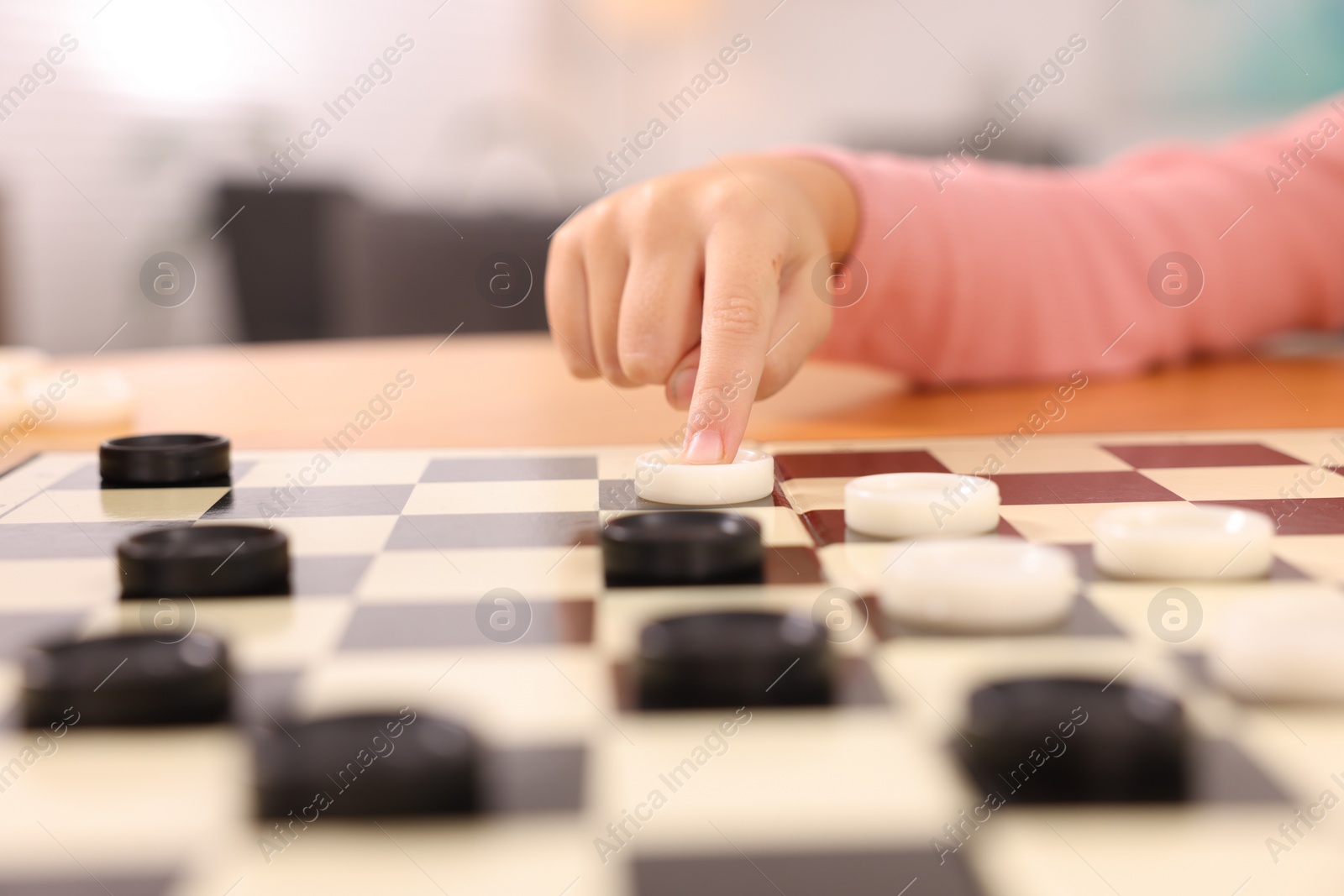 Photo of Girl playing checkers at table indoors, closeup