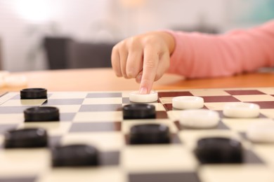 Girl playing checkers at table indoors, closeup