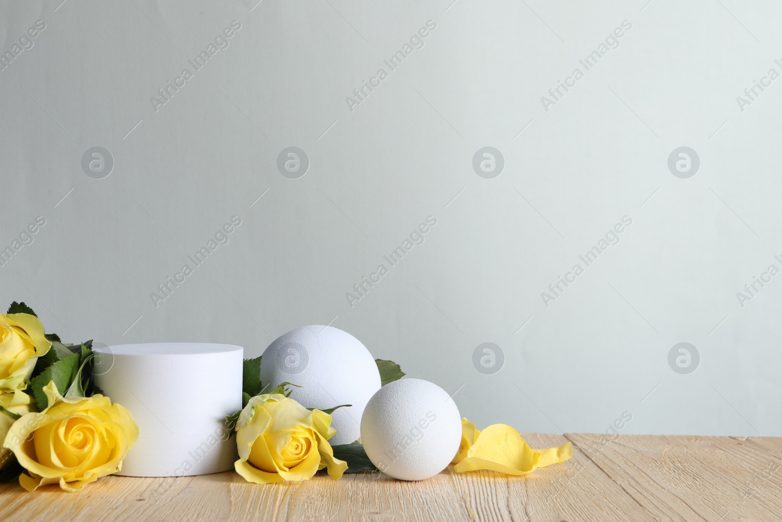 Photo of Beautiful presentation for product. White geometric figures and yellow roses on wooden table against light grey background, space for text