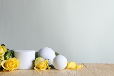 Beautiful presentation for product. White geometric figures and yellow roses on wooden table against light grey background, space for text