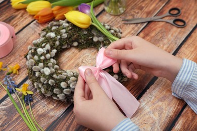 Woman decorating willow wreath with pink bow at wooden table, closeup