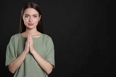 Photo of Woman with clasped hands praying on black background, space for text