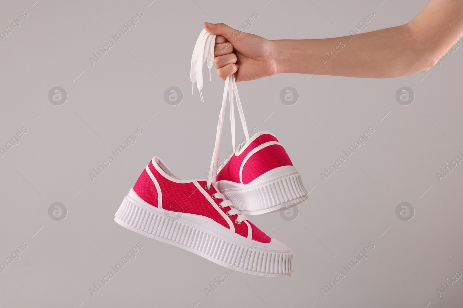 Photo of Woman holding pair of classic old school sneakers on light grey background, closeup