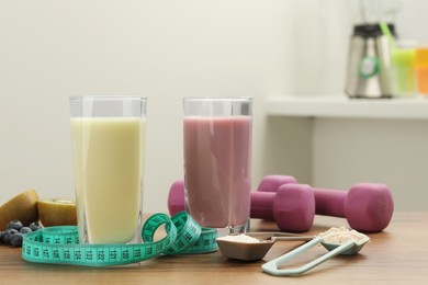 Photo of Tasty shakes, measuring tape, different powders and dumbbells on wooden table indoors. Weight loss