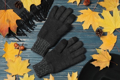 Flat lay composition with stylish woolen gloves and autumn decor on blue wooden table