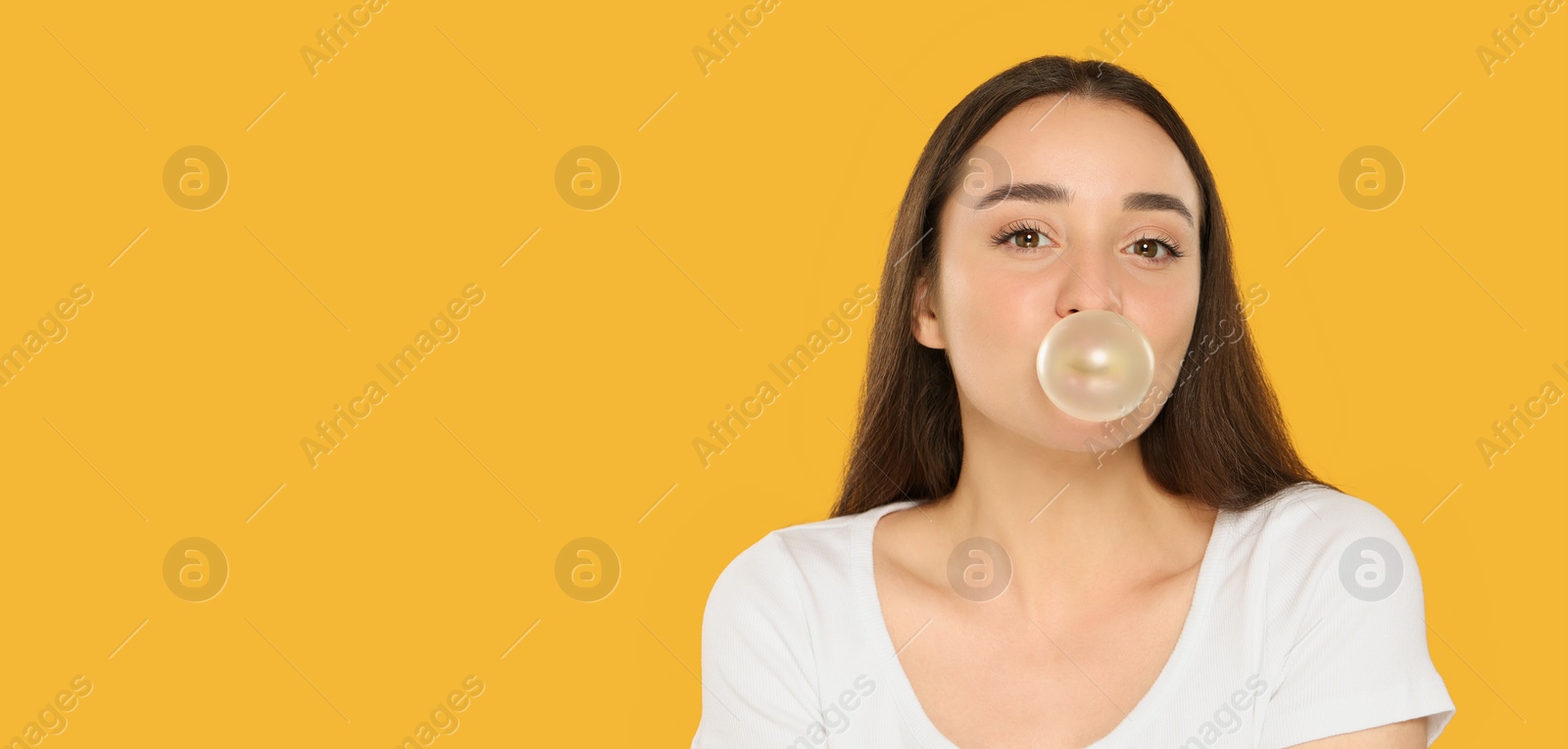 Photo of Beautiful young woman blowing bubble gum on yellow background