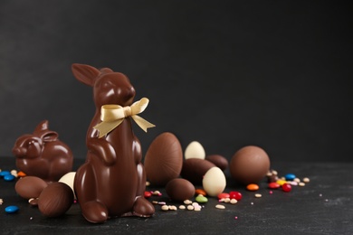 Photo of Chocolate Easter bunnies, eggs and candies on black table. Space for text