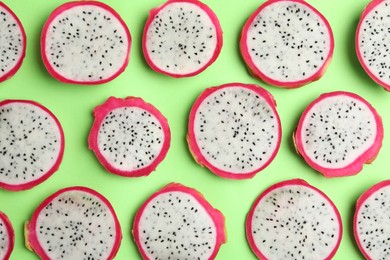 Slices of delicious dragon fruit (pitahaya) on green background, flat lay