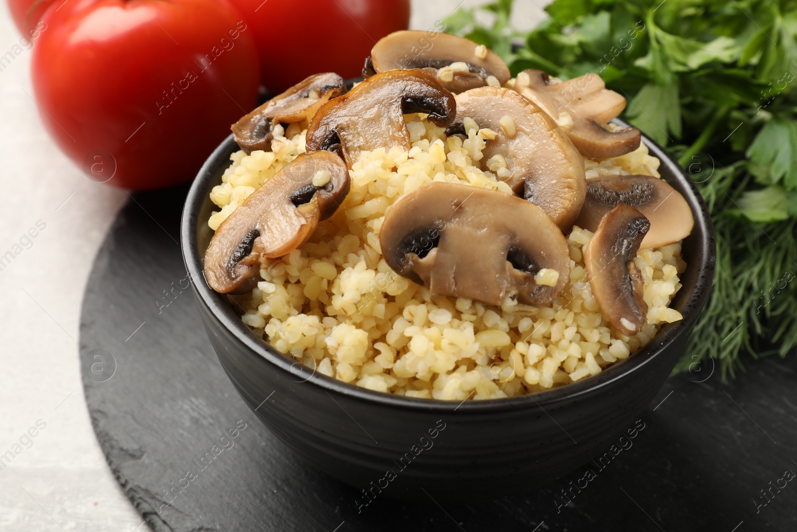 Photo of Delicious bulgur with mushrooms in bowl on table, closeup