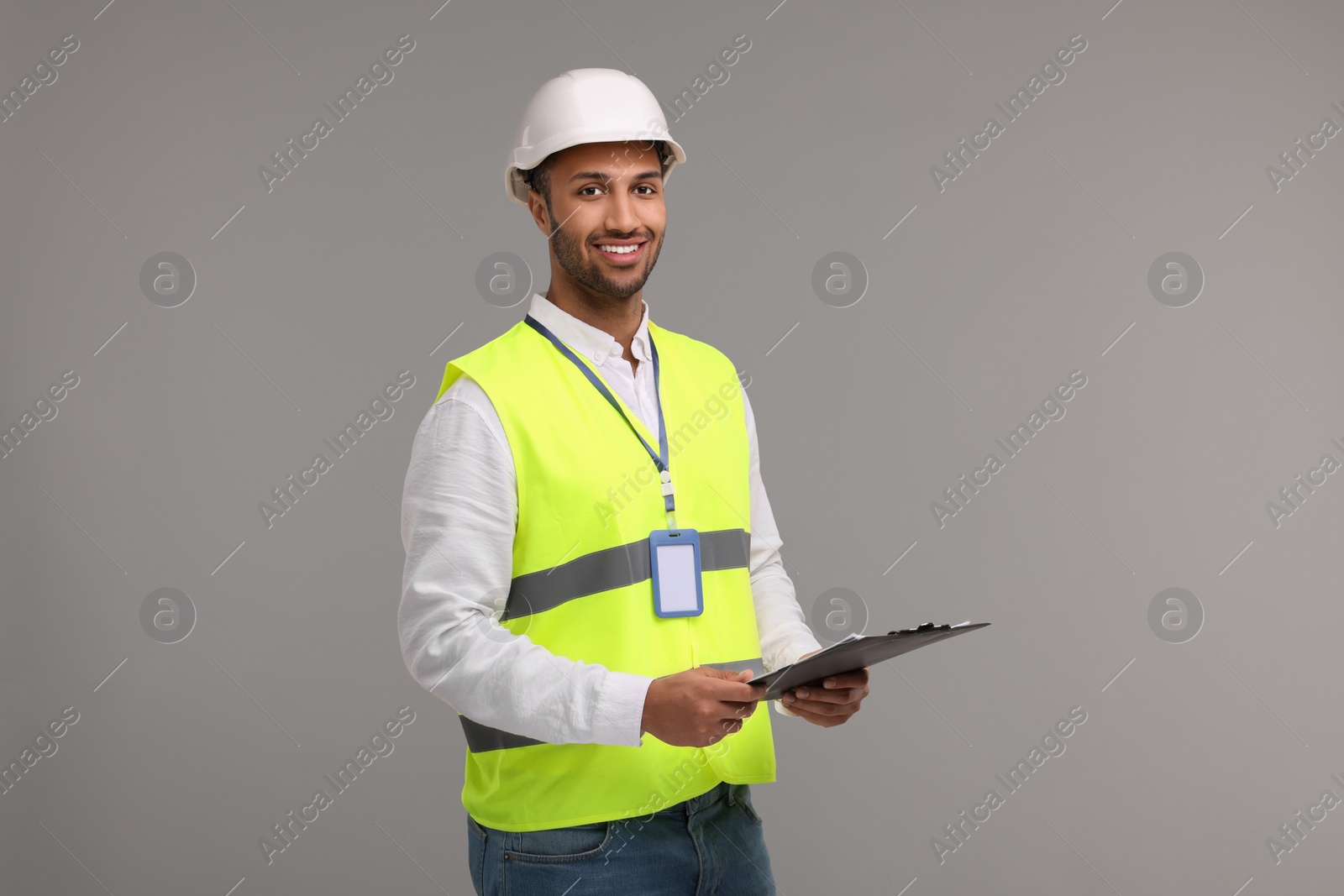 Photo of Engineer in hard hat holding clipboard on grey background