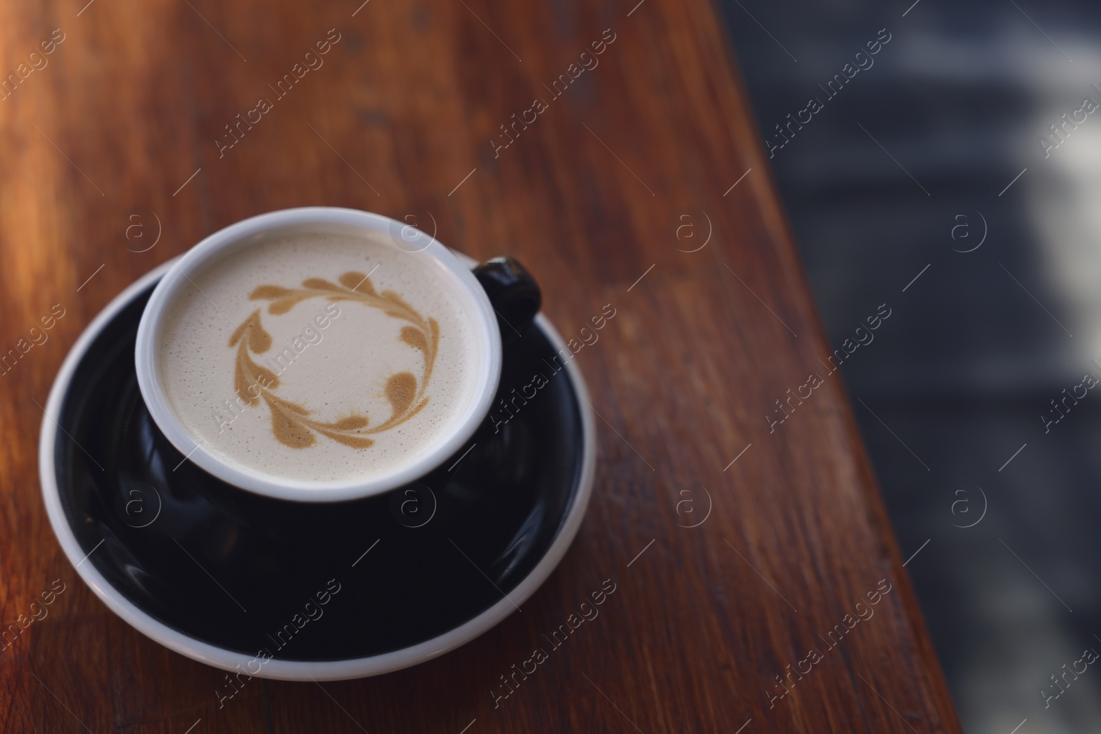 Photo of Ceramic cup of aromatic coffee with foam on wooden table in outdoor cafe. Space for text