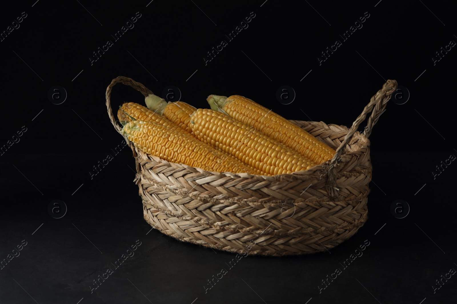 Photo of Corn cobs in basket on black table