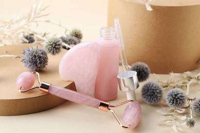 Composition with rose quartz gua sha tool, facial roller and bottle of serum on beige background
