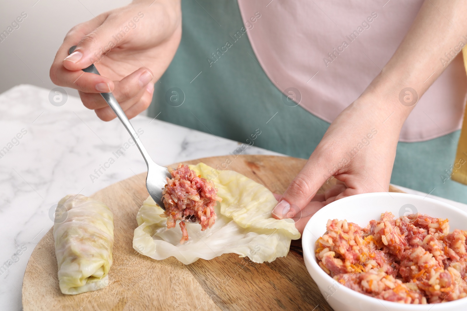 Photo of Woman preparing stuffed cabbage roll at white marble table, closeup