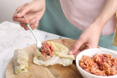 Woman preparing stuffed cabbage roll at white marble table, closeup