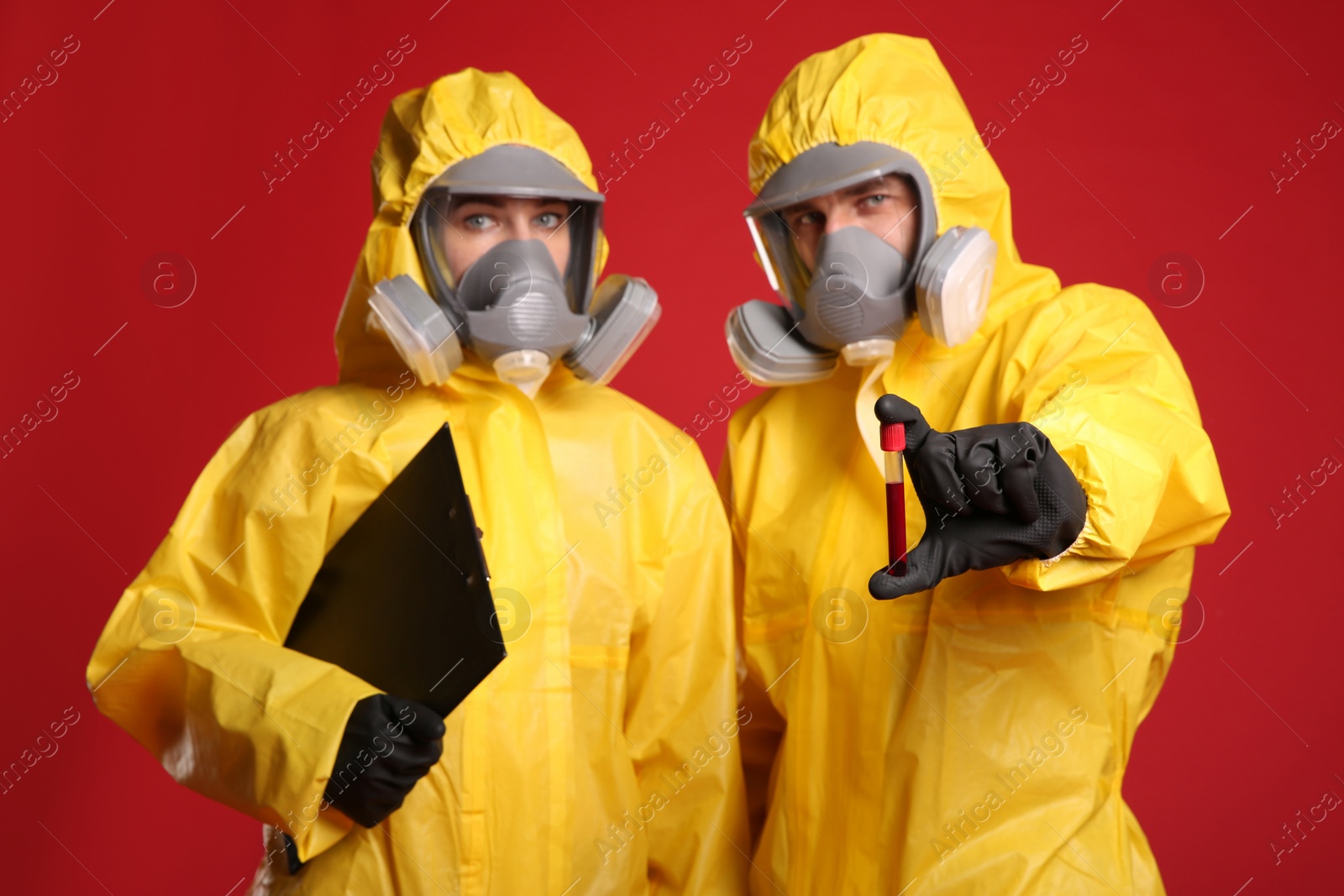 Photo of People in chemical protective suits with blood sample and clipboard on red background. Virus research