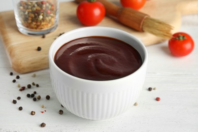 Photo of Composition with bowl of barbecue sauce on white wooden table