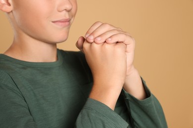 Photo of Boy with clasped hands praying on beige background, closeup