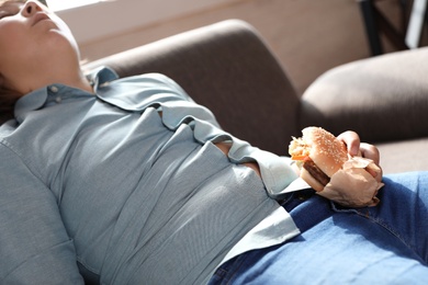 Photo of Overweight boy with burger sleeping on sofa at home