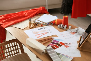 Photo of Sketches of fashion clothes and thread supplies at designer's workplace indoors