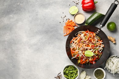 Photo of Shrimp stir fry with noodles and vegetables in wok surrounded by ingredients on grey table, flat lay. Space for text