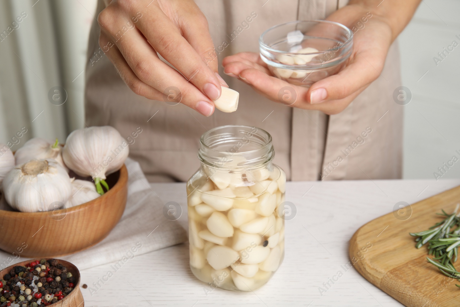 Photo of Woman taking clove of pickled garlic from jar at white wooden table in kitchen, closeup