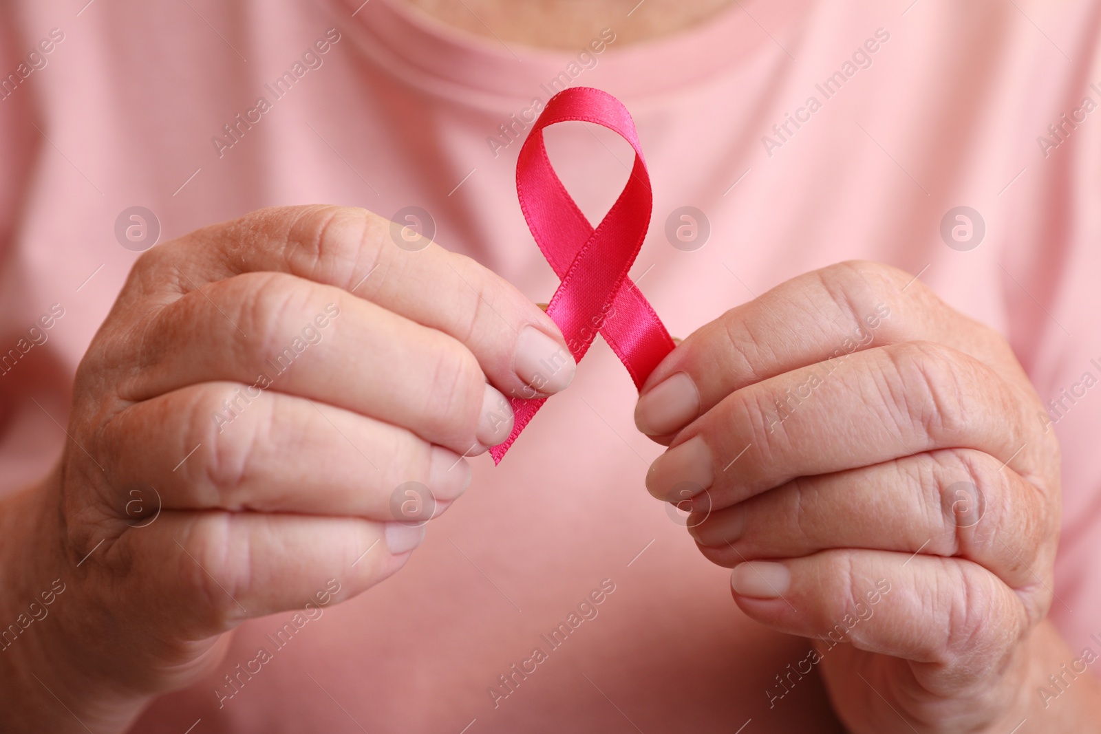 Photo of Senior woman holding pink ribbon, closeup. Breast cancer awareness