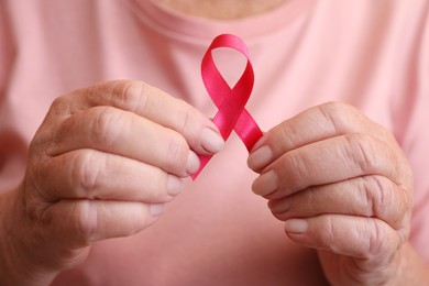 Photo of Senior woman holding pink ribbon, closeup. Breast cancer awareness