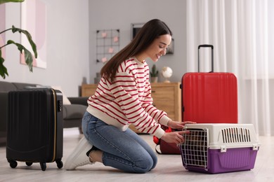 Photo of Smiling woman preparing to travel with dog indoors. Suitcases and pet carrier around her