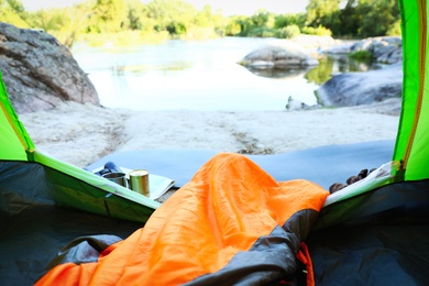 Camping tent with sleeping bag near lake, view from inside