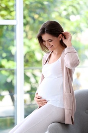 Happy pregnant woman near window at home