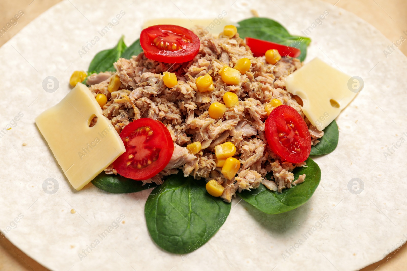 Photo of Delicious tortilla with tuna, vegetables and cheese on parchment paper, closeup. Cooking shawarma