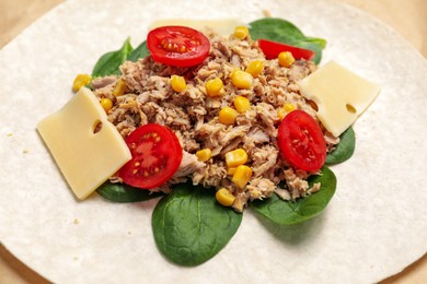 Photo of Delicious tortilla with tuna, vegetables and cheese on parchment paper, closeup. Cooking shawarma