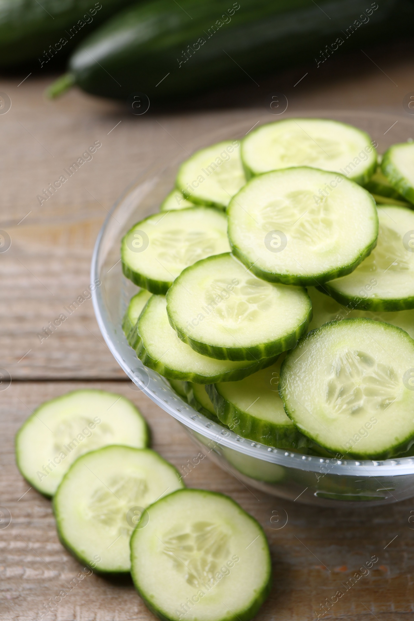 Photo of Cut cucumber in glass bowl on wooden table, closeup