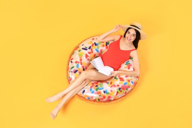 Photo of Happy young woman with beautiful suntan reading book on inflatable ring against orange background, top view