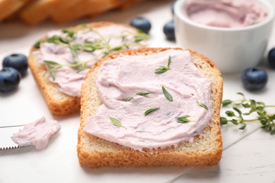 Photo of Tasty sandwiches with cream cheese, thyme and blueberries on white wooden table, closeup