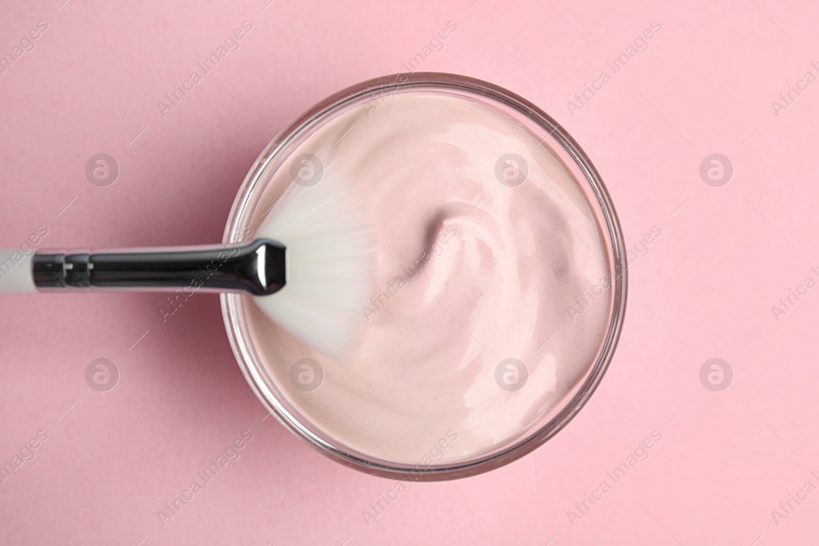 Photo of Professional face mask with brush on pink background, top view