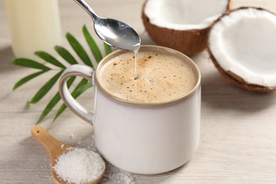 Photo of Pouring syrup into cup of coffee on white wooden table, closeup