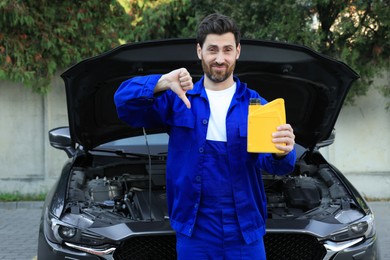 Photo of Worker holding yellow container of motor oil and showing thumbs down near car