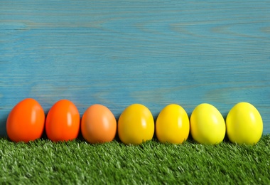 Photo of Easter eggs on green grass against light blue wooden background
