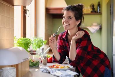 Photo of Young woman with plate of freshly fried eggs and vegetables at countertop in kitchen