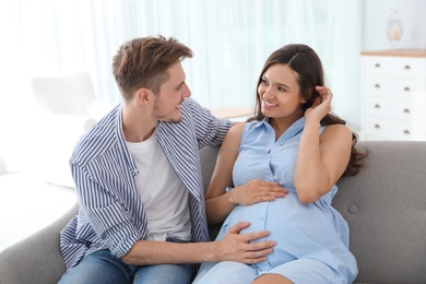 Young man and his pregnant wife sitting on sofa at home