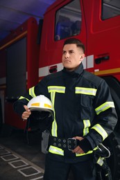 Photo of Portrait of firefighter in uniform with helmet near fire truck at station